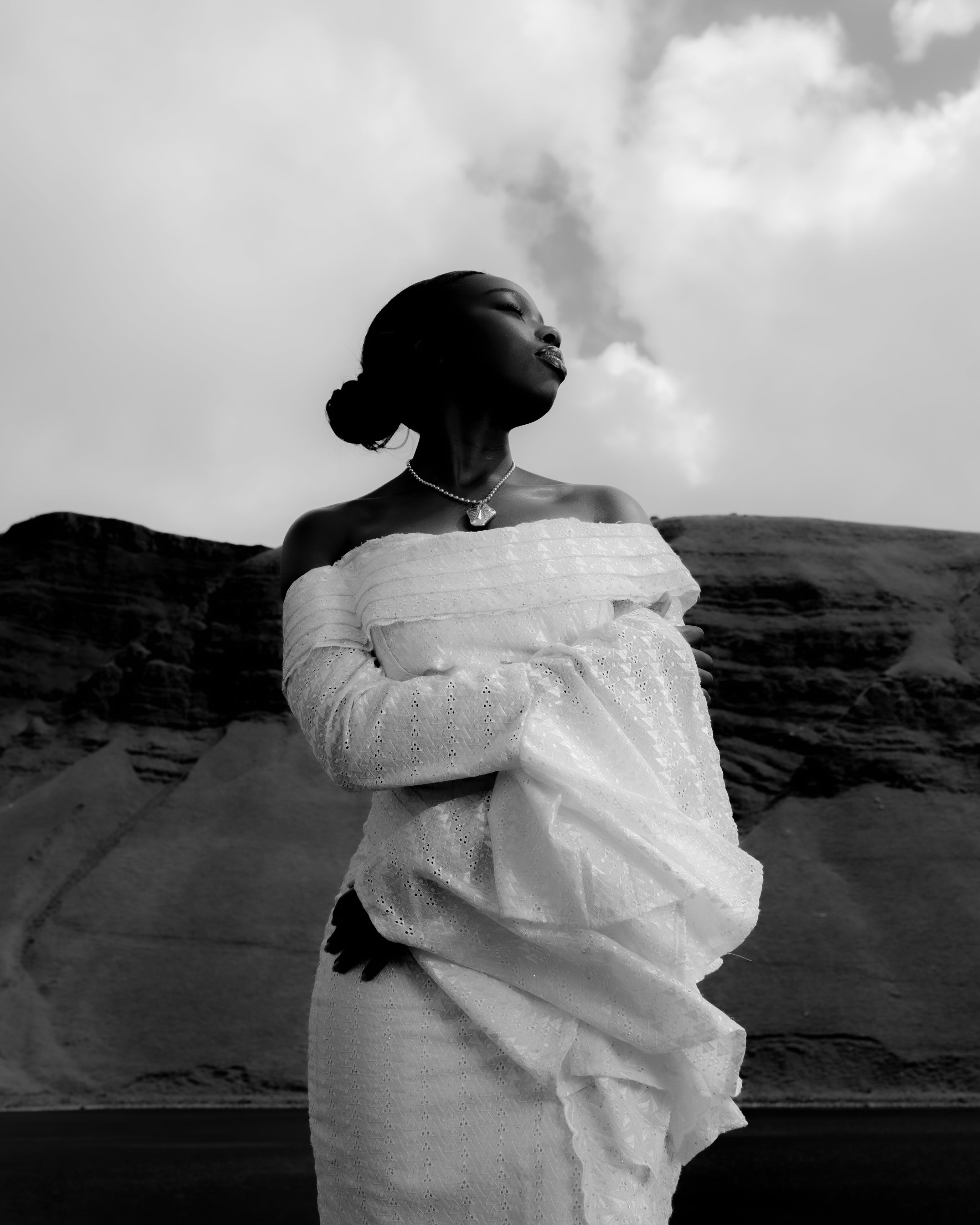 Senegalese woman in an off-shoulder white dress wearing Maison Nwar jewelry, standing proudly in the Welsh mountains black and white editorial photography.