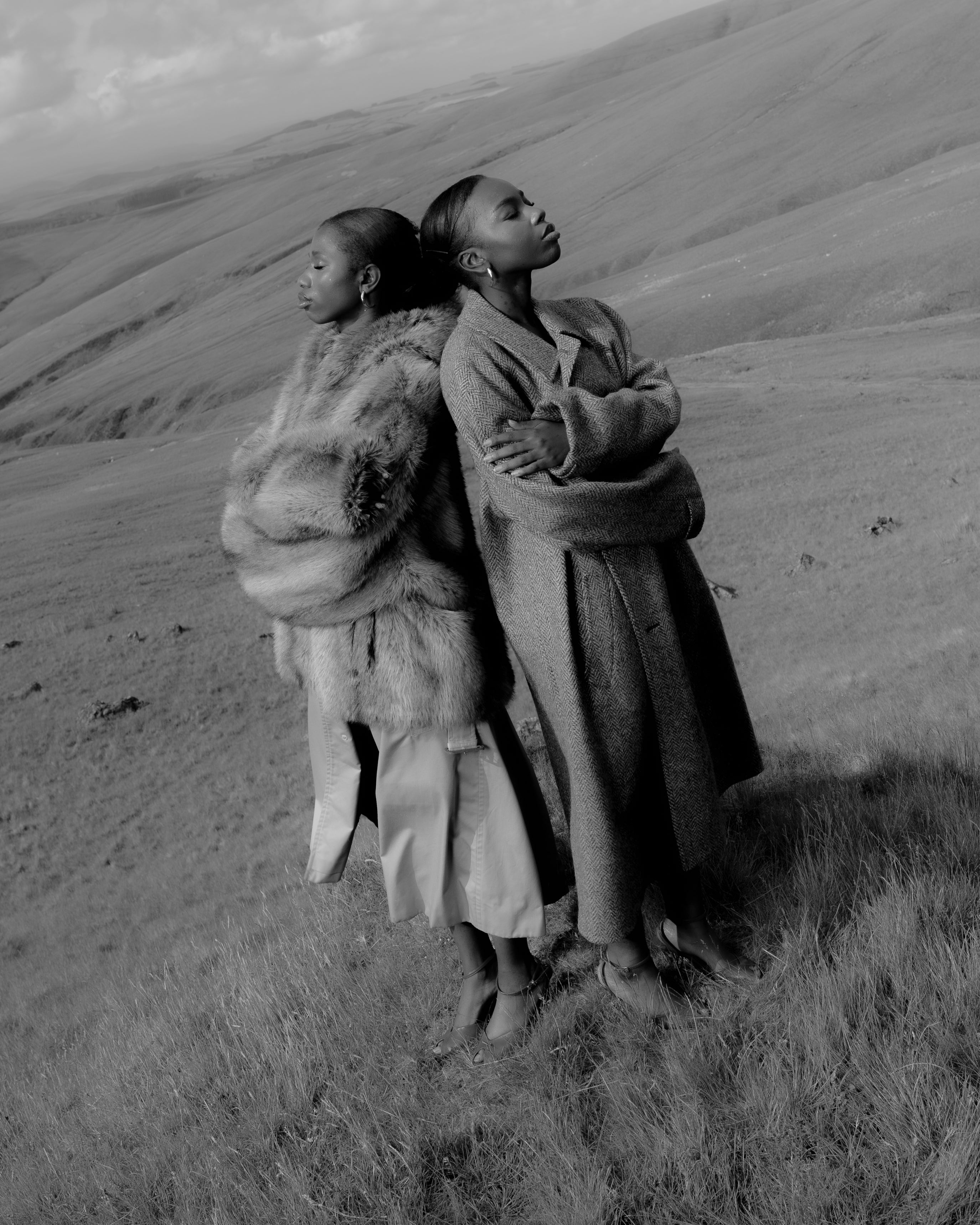 Two Senegalese sisters in long textured coats, standing together on the Welsh mountains Maison Nwar black and white editorial photography.