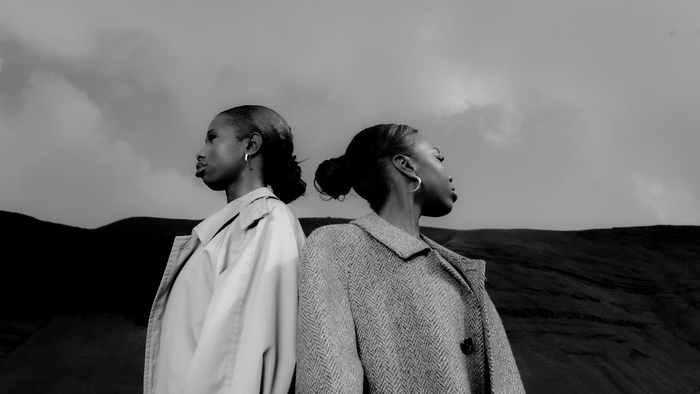 Two Senegalese women in textured coats, standing in silence atop a Welsh mountain Maison Nwar editorial shoot.