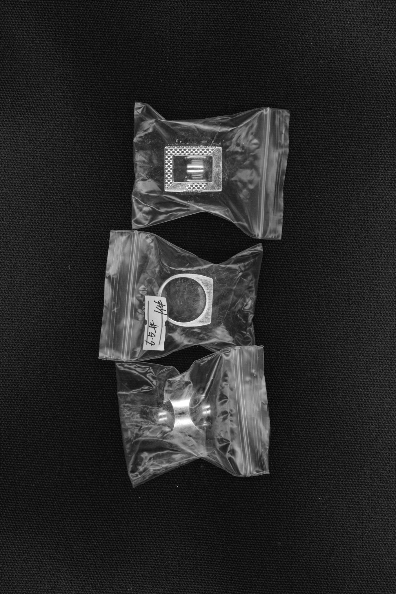 Three pieces of silver jewelry in clear plastic bags on a black surface.