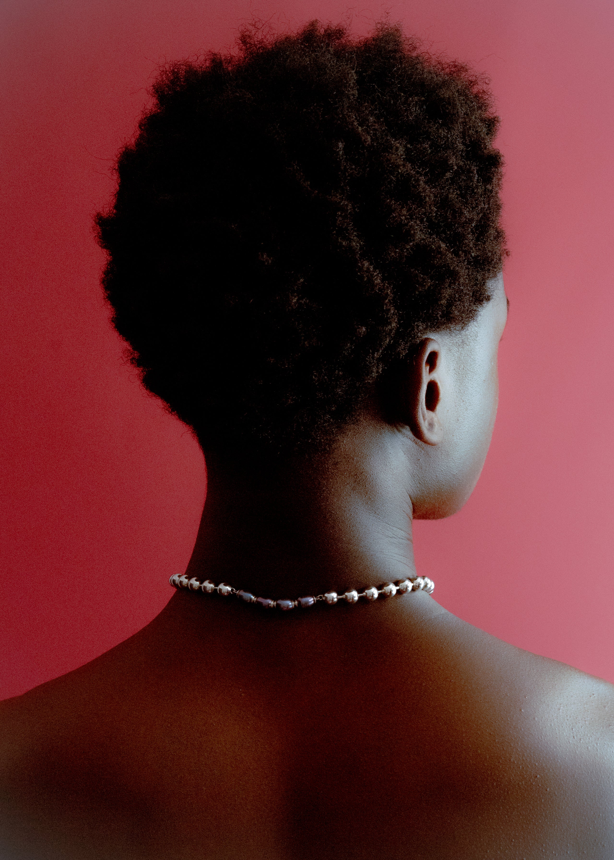 Rear view portrait of a person wearing a pearl necklace against a deep red background