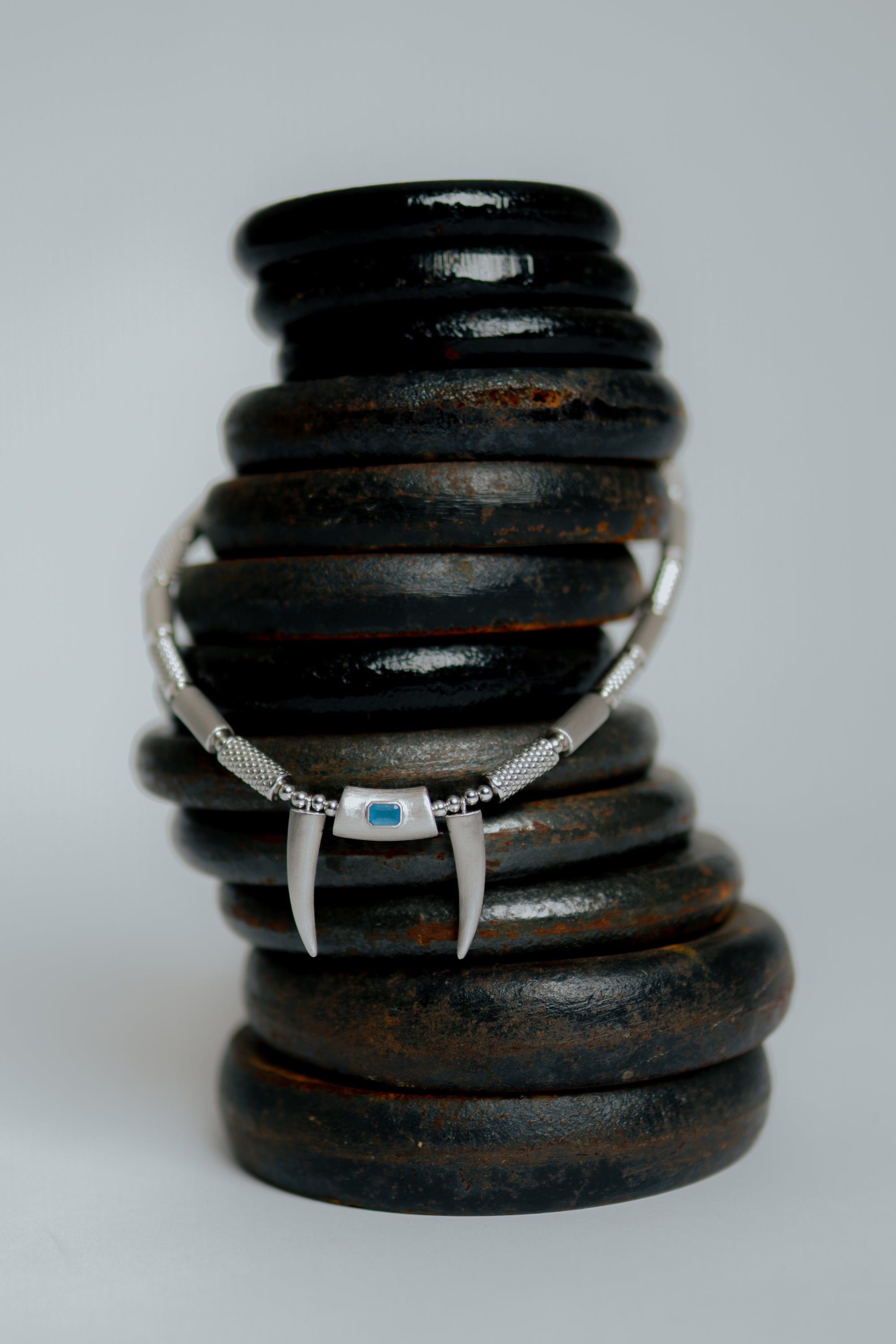 Necklace with a blue stone pendant and claw details placed on stacked dark objects.