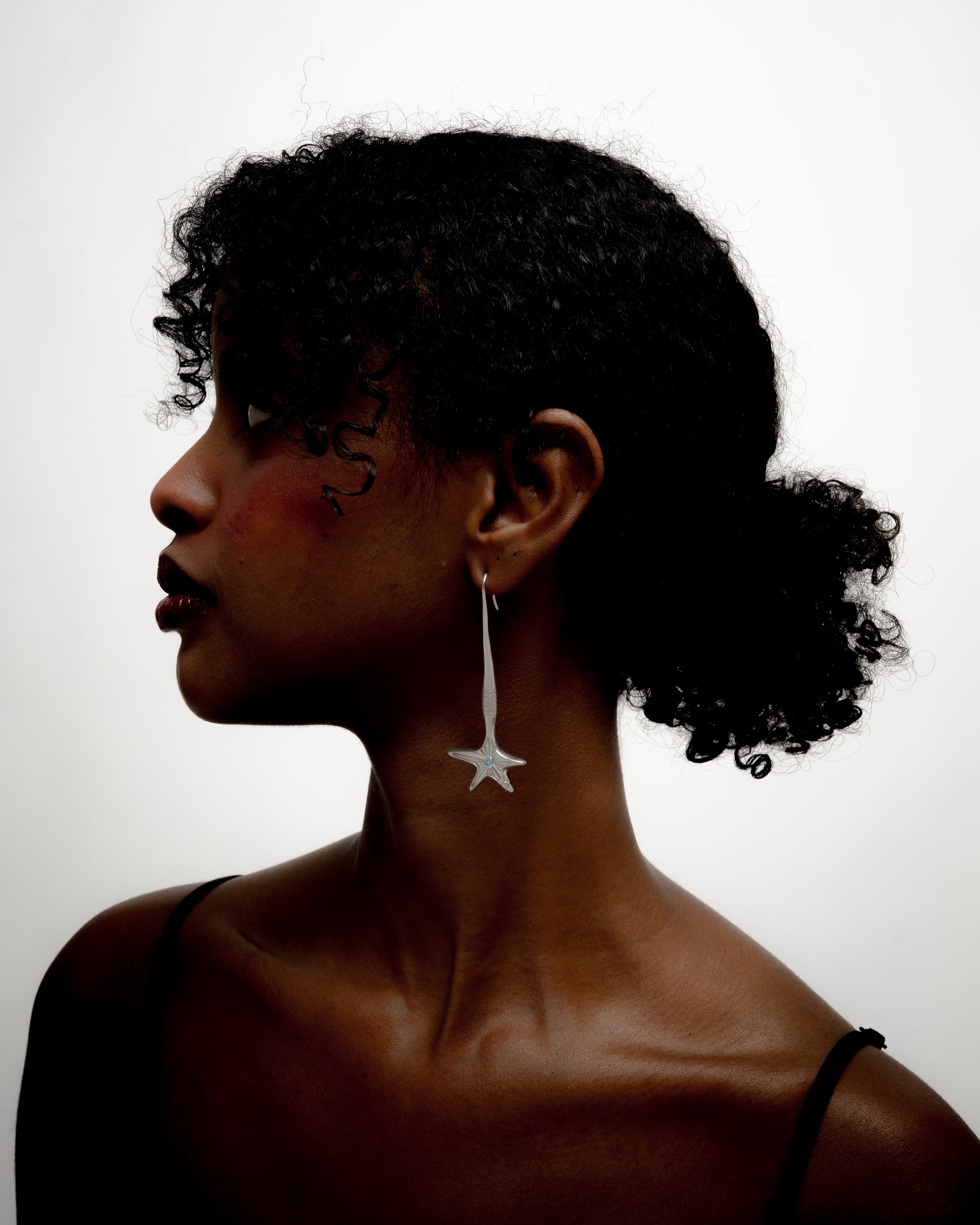Person in profile wearing a long star earring against a white background.