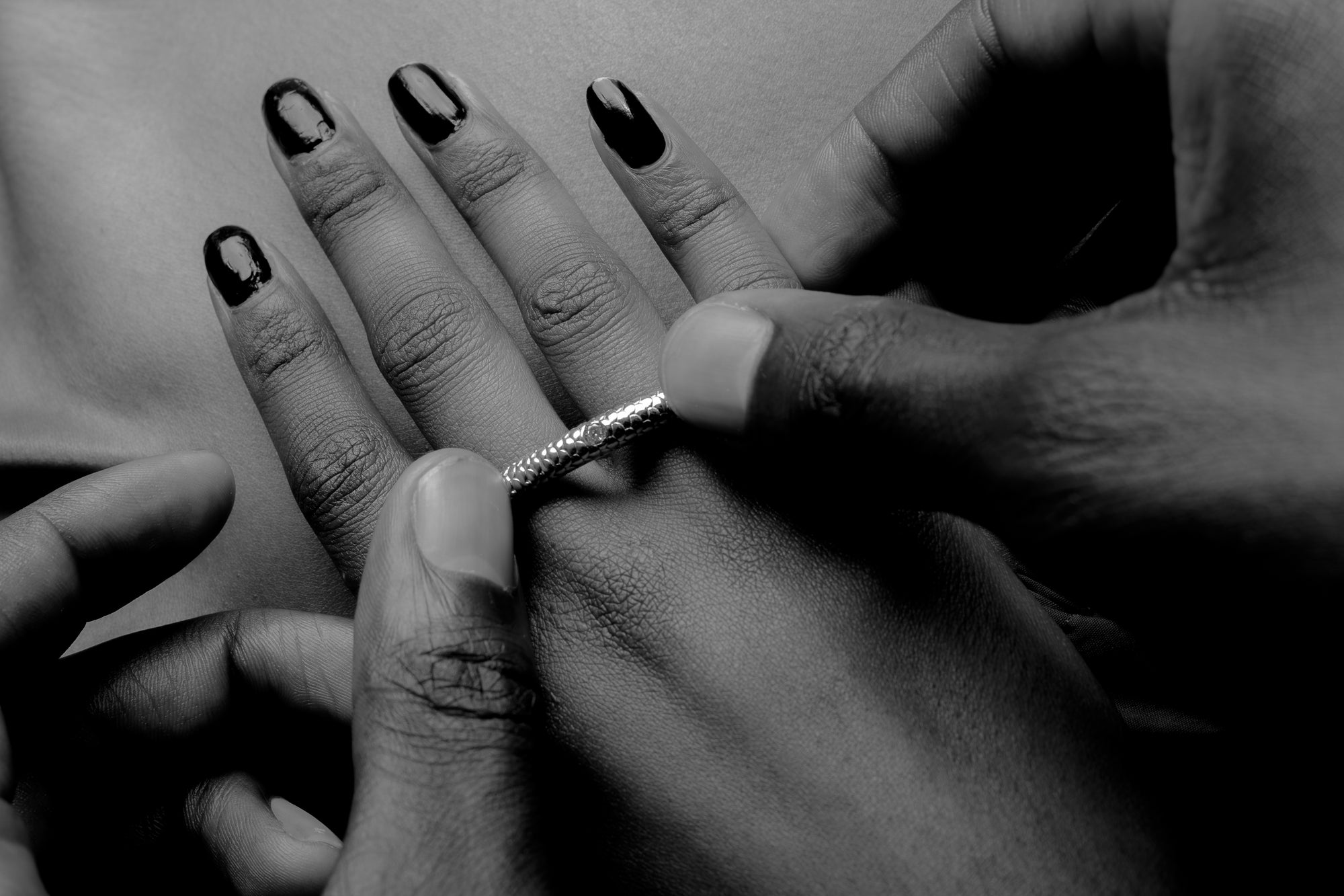 Hands placing a textured silver ring onto a finger.