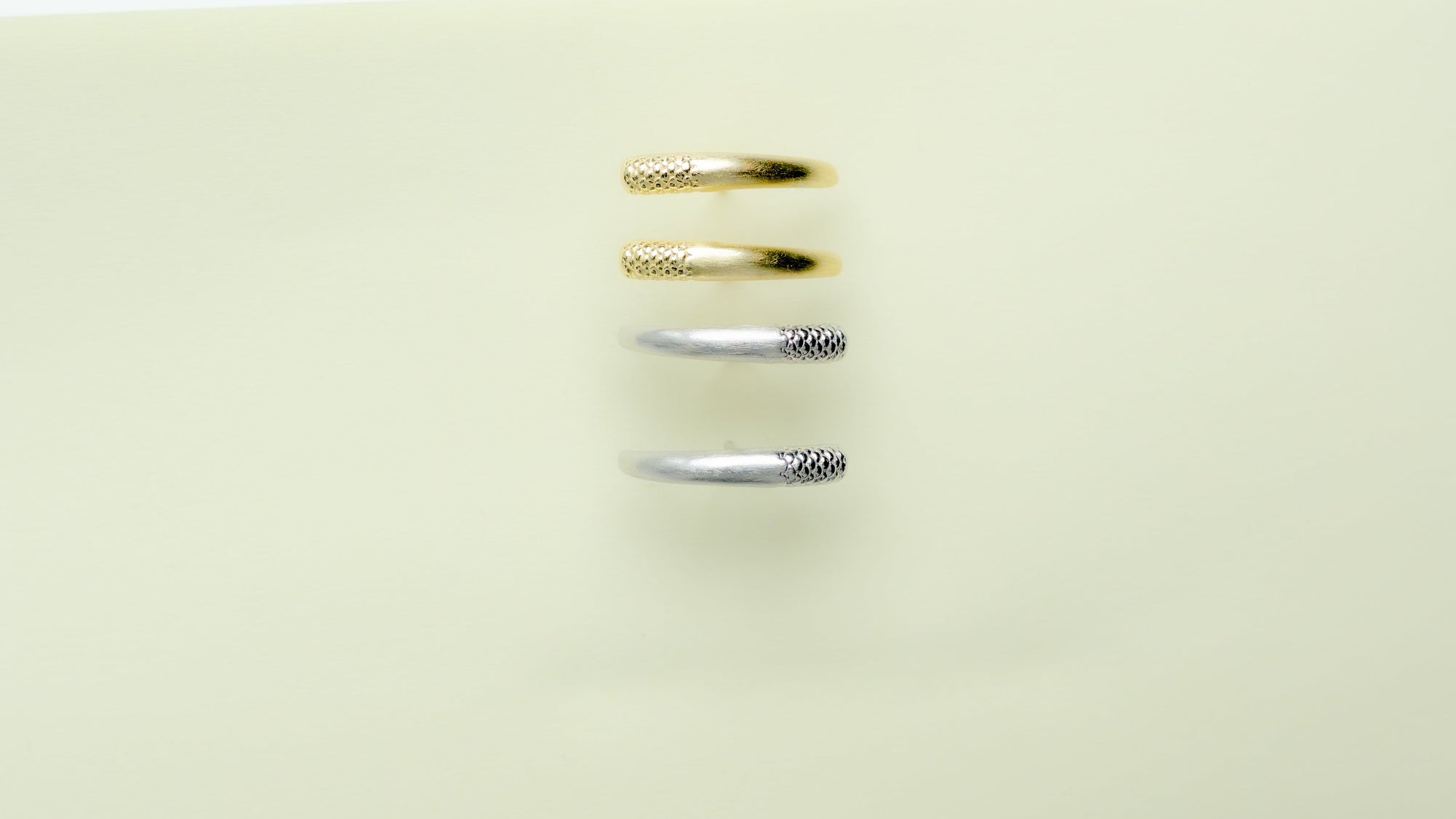 Four rings in gold and silver finishes aligned vertically on a light background.