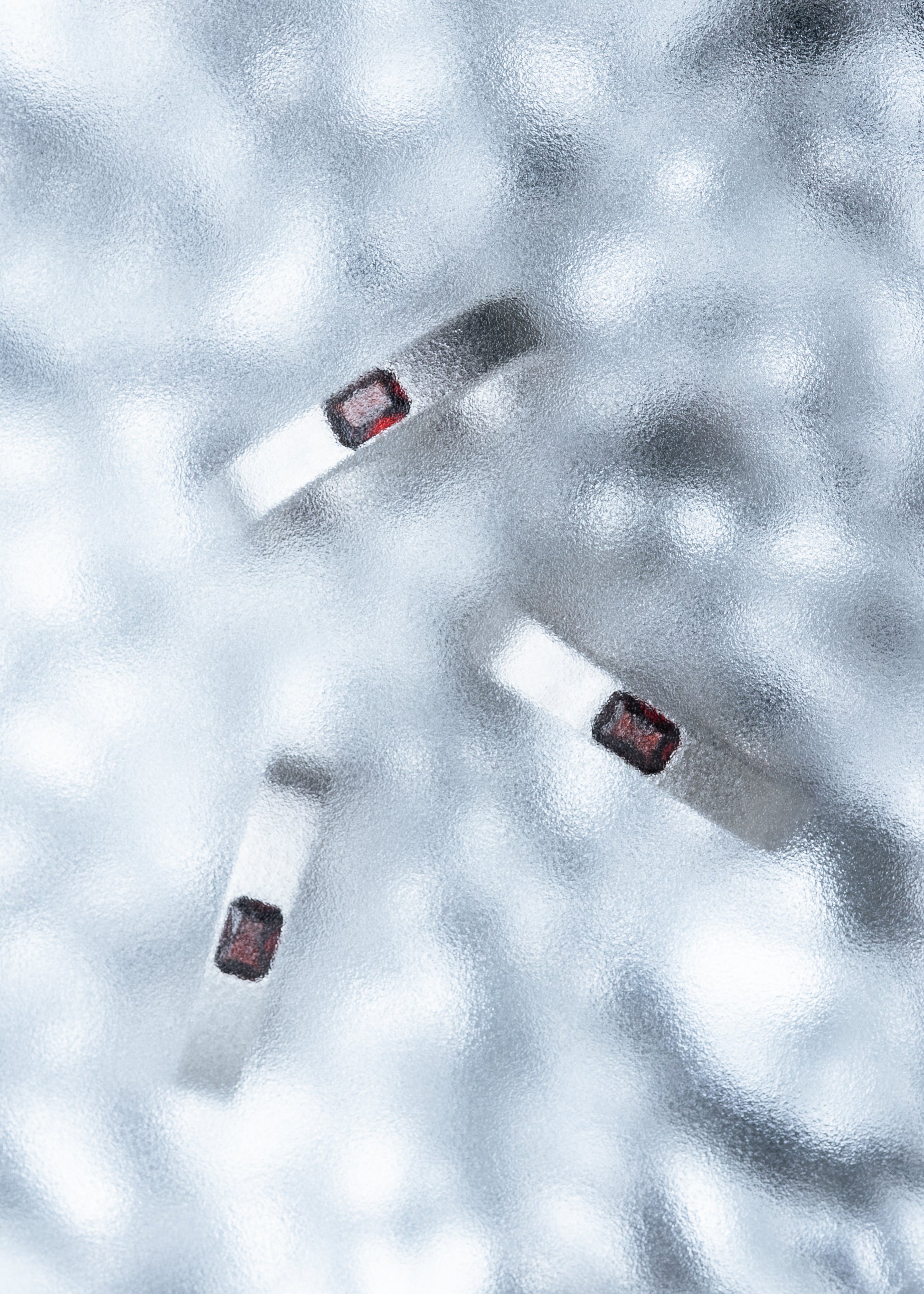 Three silver rings with red stones arranged on a textured icy surface