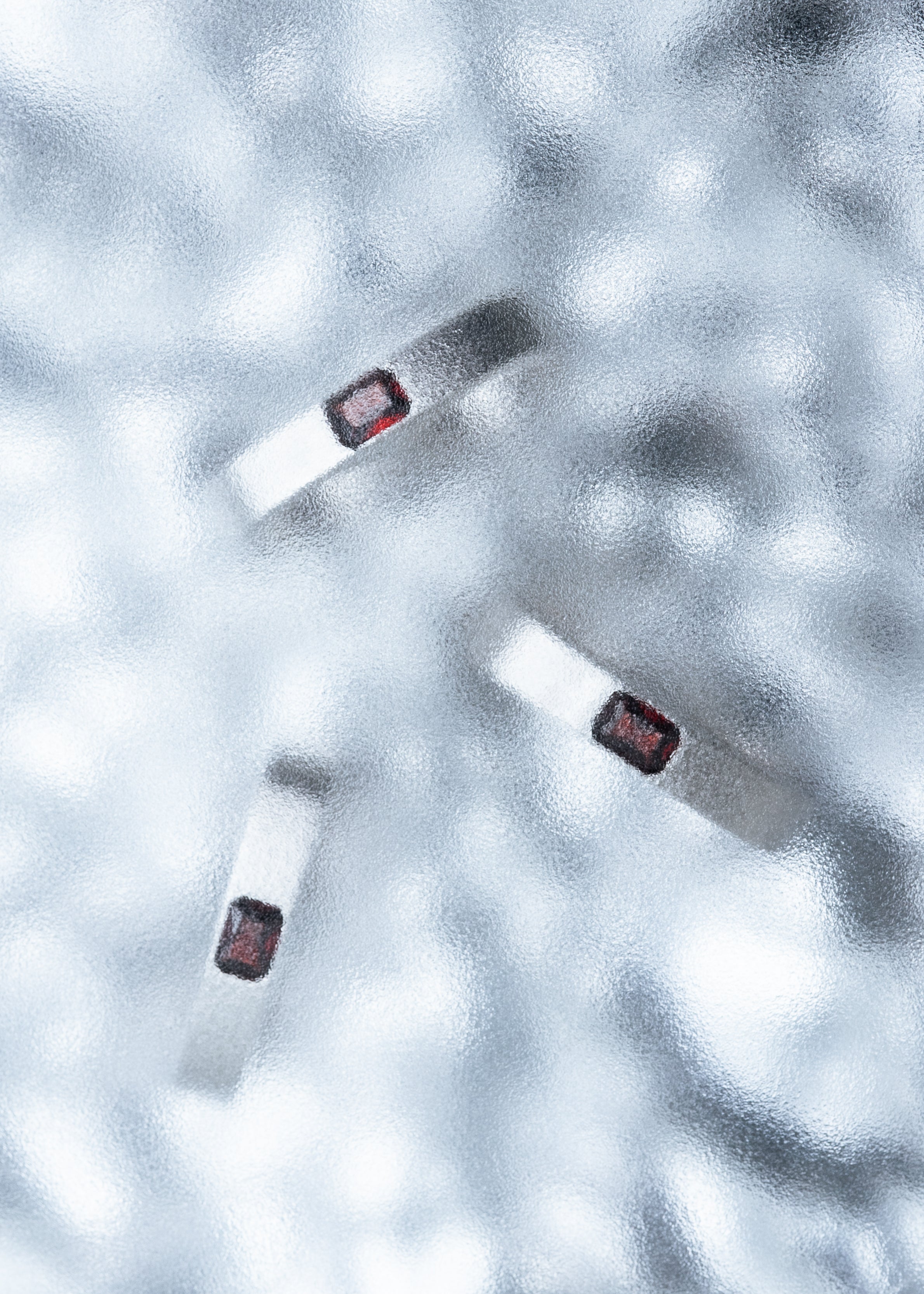 Three silver rings with red stones arranged on a textured icy surface