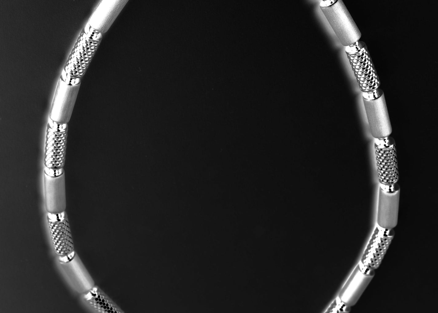 Close-up of a silver bracelet with textured segments on a black background.