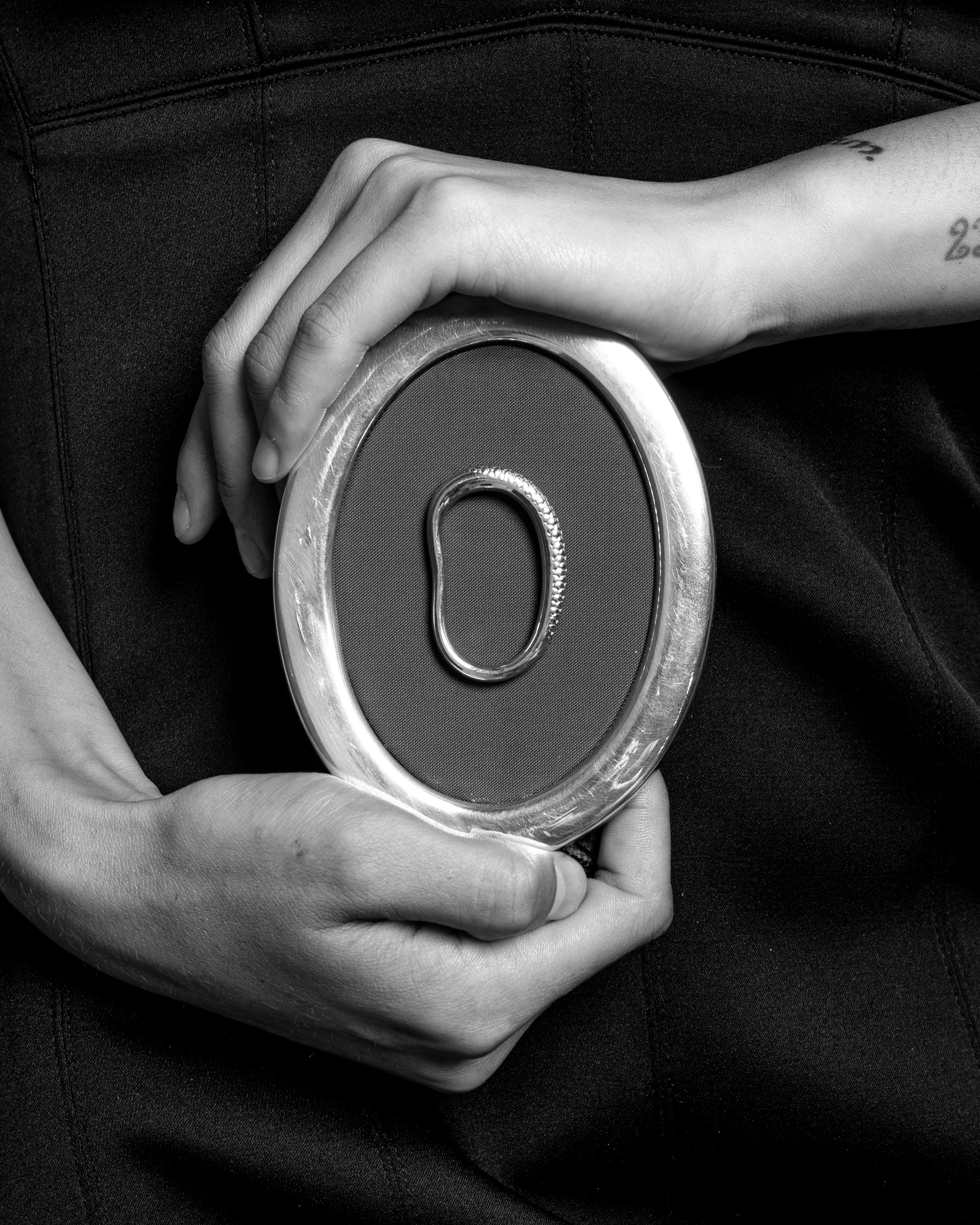 Hands holding a circular metal object with a silver ring at the center on a dark background.