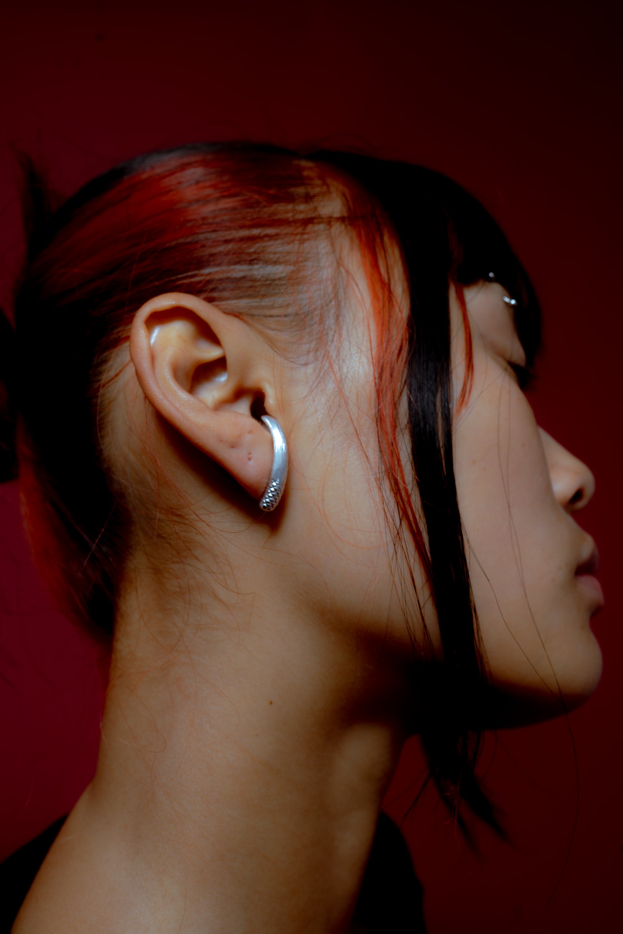 Side profile of a person wearing a small gold hoop earring against a light background.