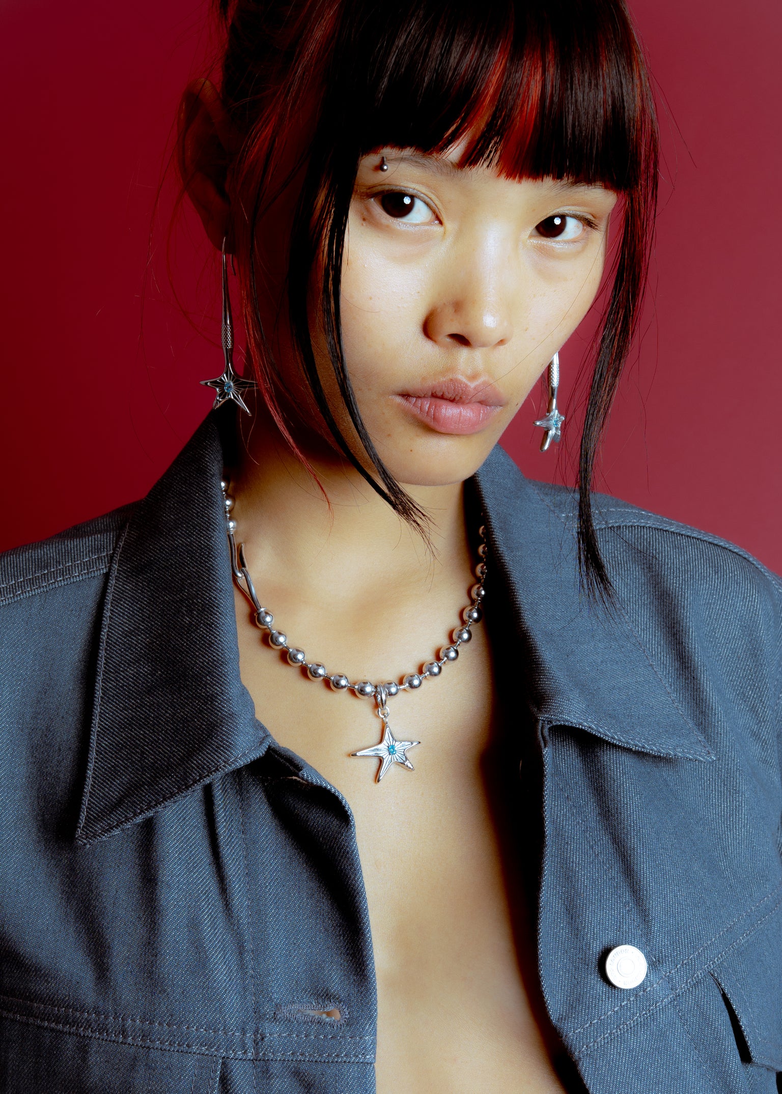 Model wearing Maison Nwar star pendant necklace, editorial portrait on burgundy background
