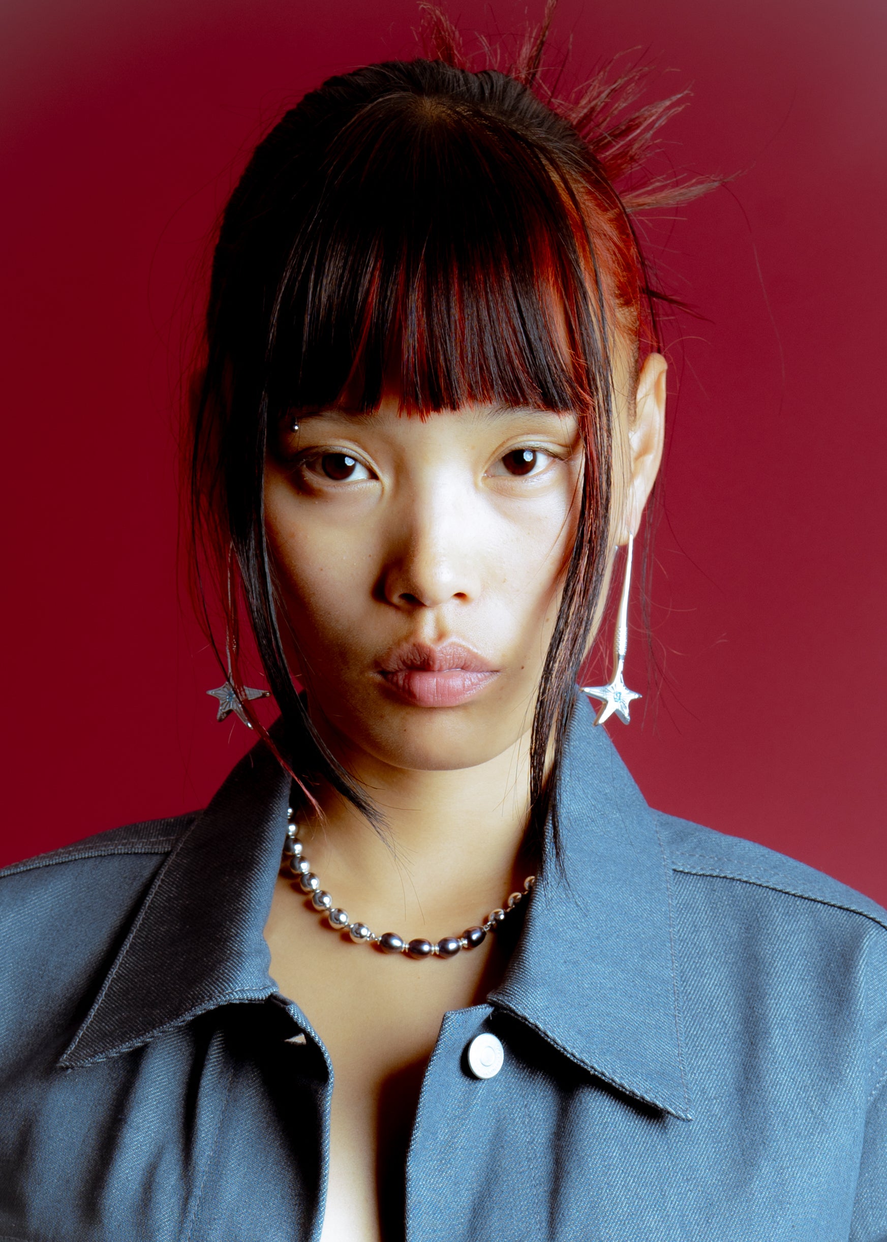 Portrait of a woman wearing silver star earrings and a beaded necklace against a deep red background