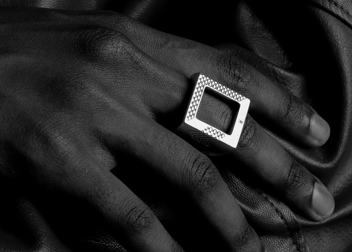 Close-up of a hand wearing a square silver ring on dark fabric.