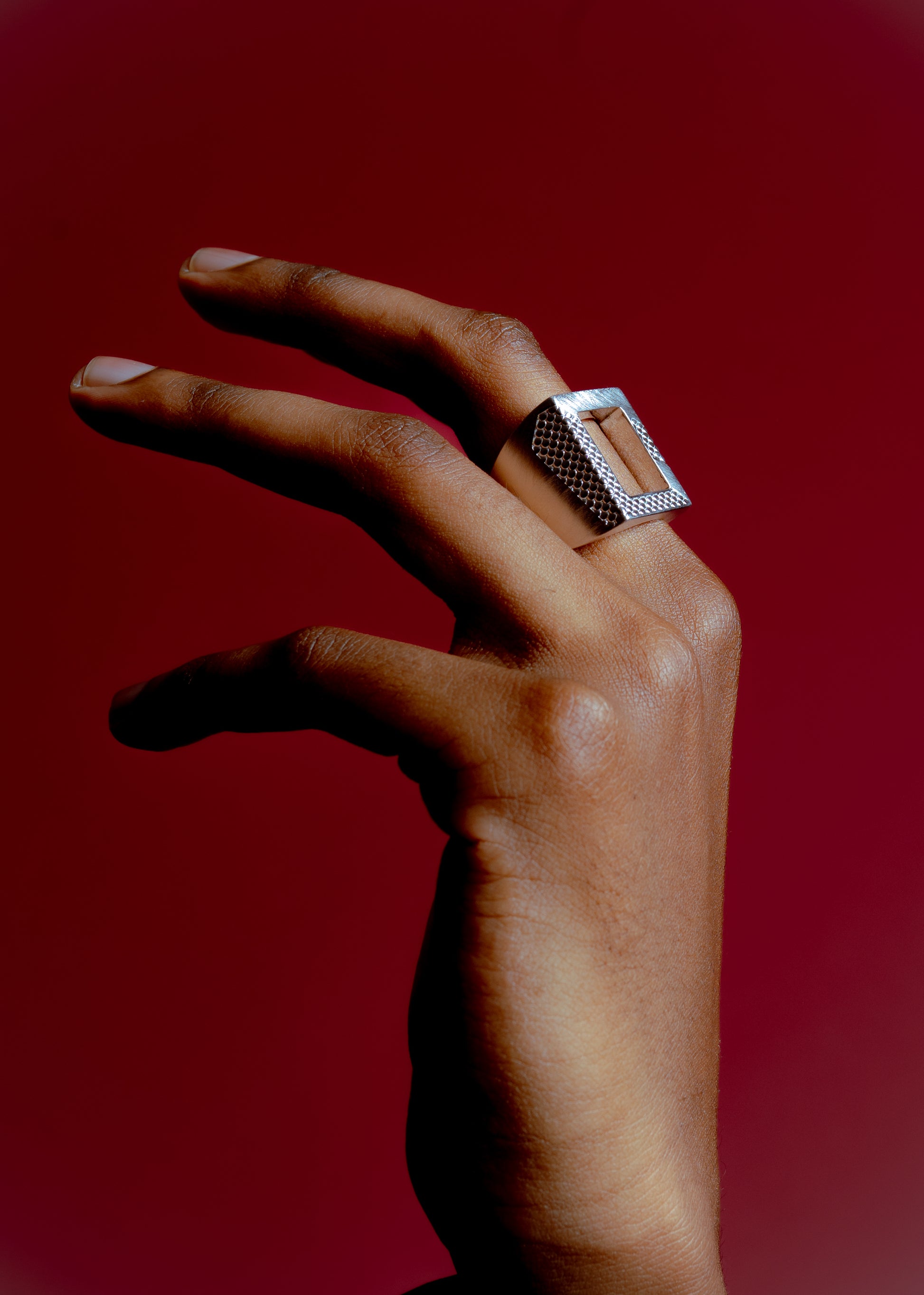 Hand wearing Maison Nwar ring against burgundy background, close-up