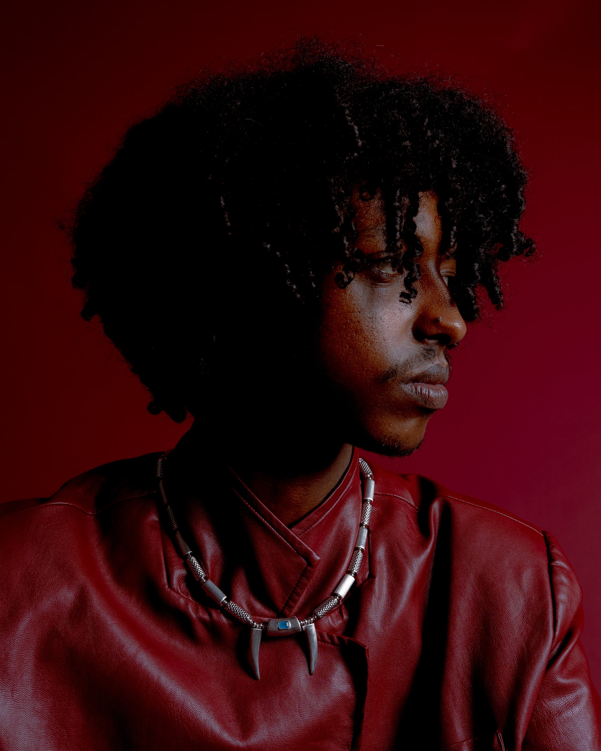 Person in a red outfit wearing a necklace with pendants against a red background.