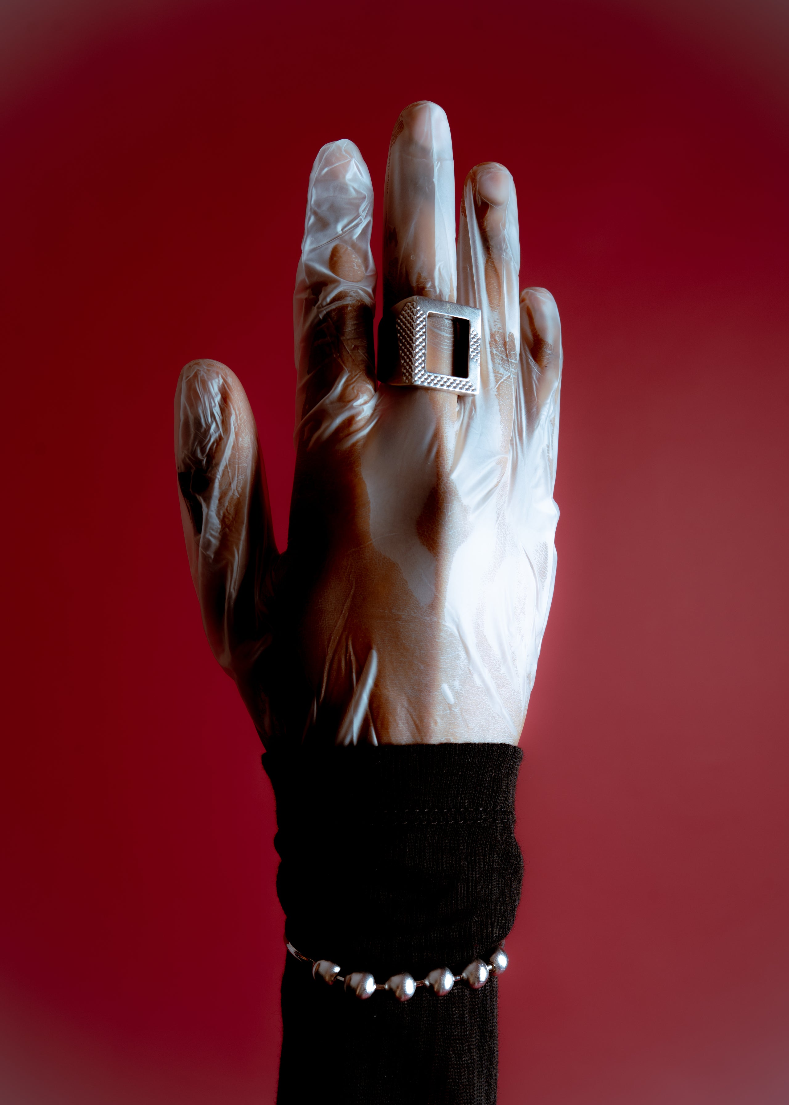 Gloved hand wearing a silver ring against a red background