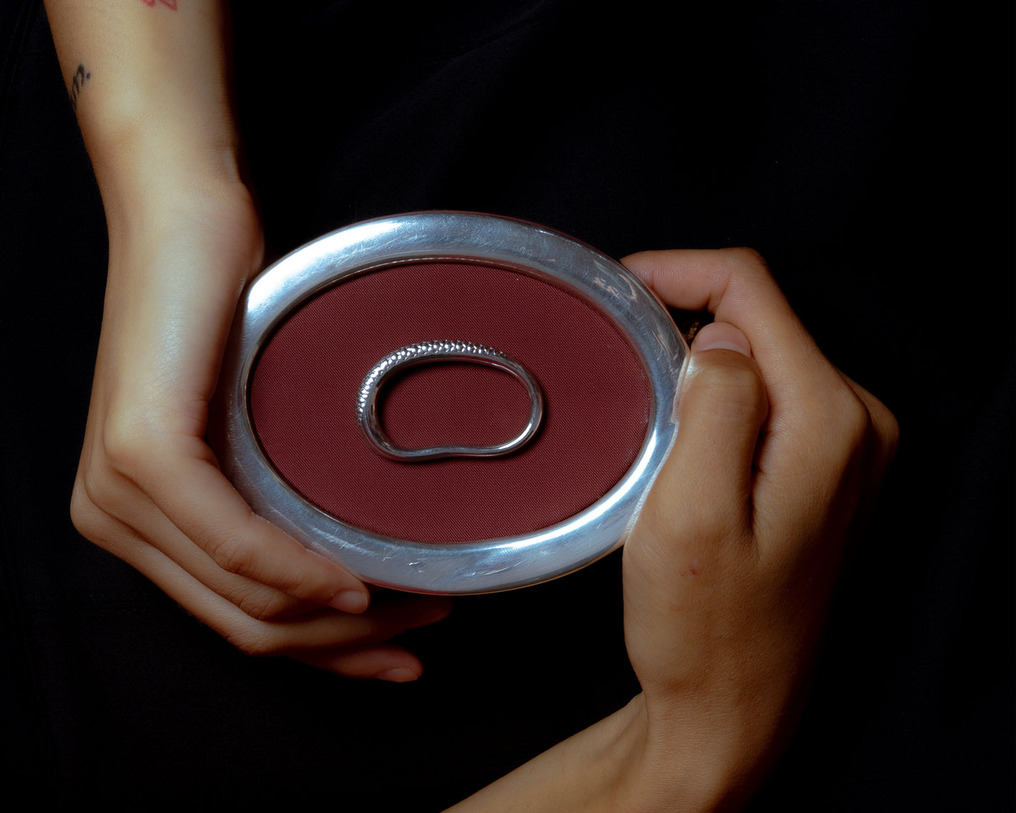 Hands holding a silver ring placed on a red circular surface.