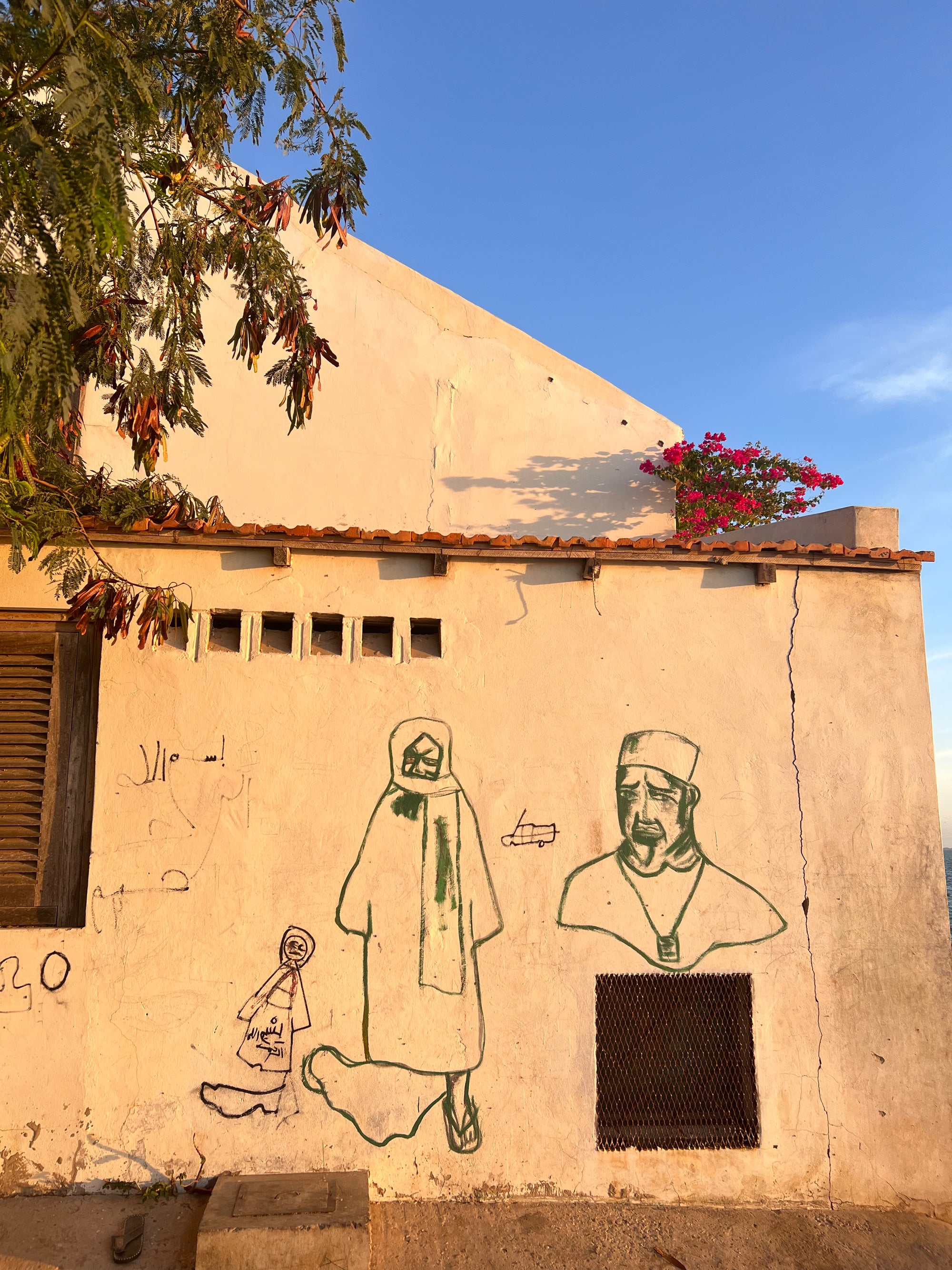 Exterior wall with drawn figures and street art under a clear blue sky.