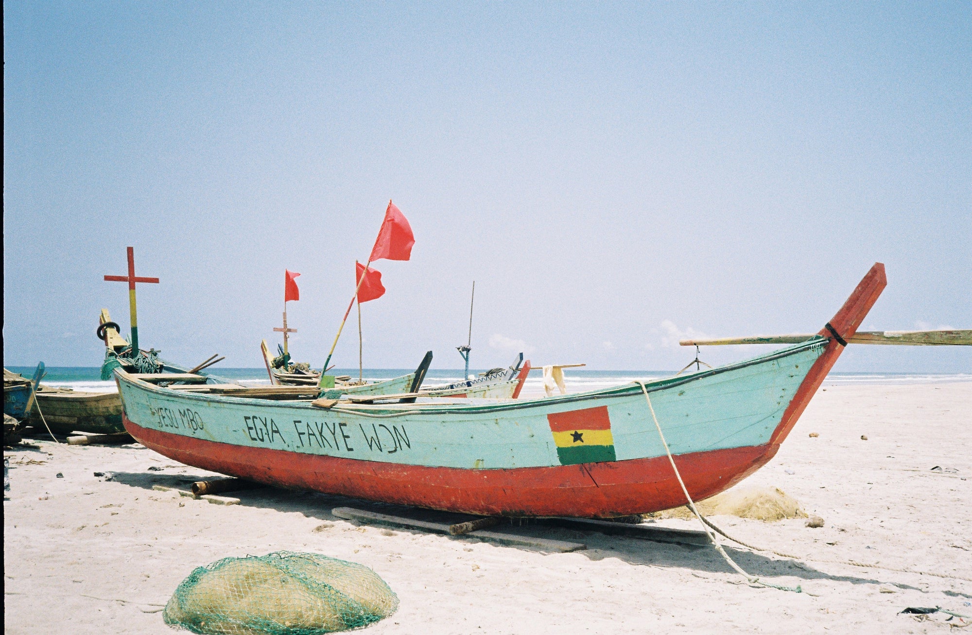 Fishing boat on a sandy beach with flags and markings under a clear sky.