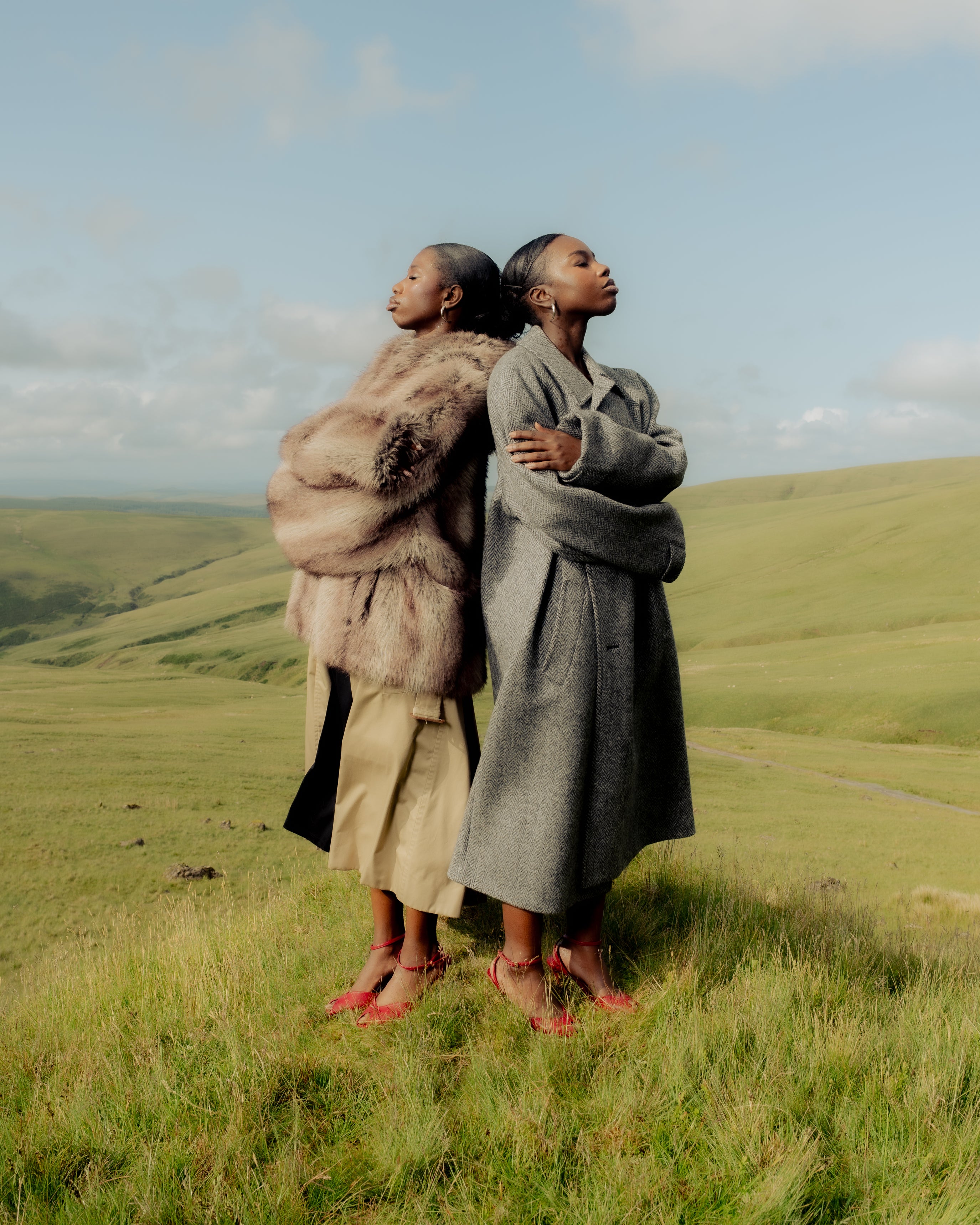 Two Senegalese sisters wearing textured coats, standing together in the Welsh hills — Maison Nwar editorial photography