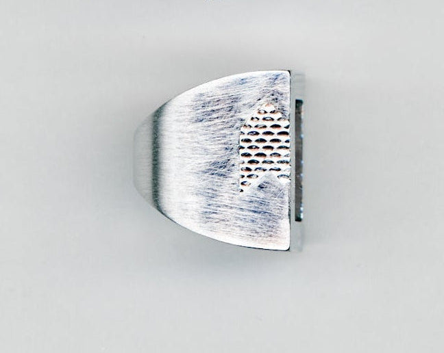 Silver ring with brushed finish and textured detail on a light background.