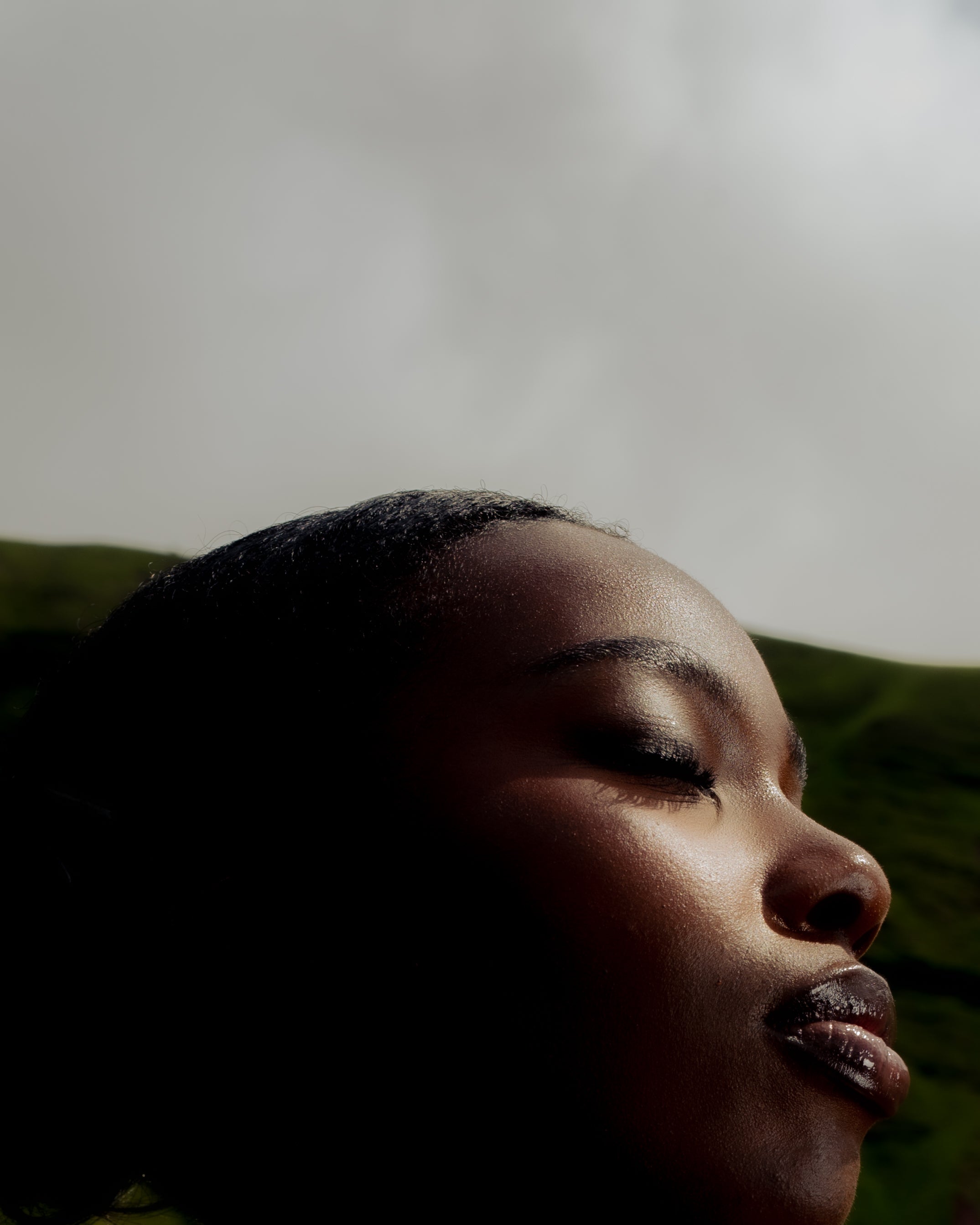Close-up portrait of a Senegalese woman with eyes closed, her skin glowing in natural light against the Welsh hills  Maison Nwar editorial photography.