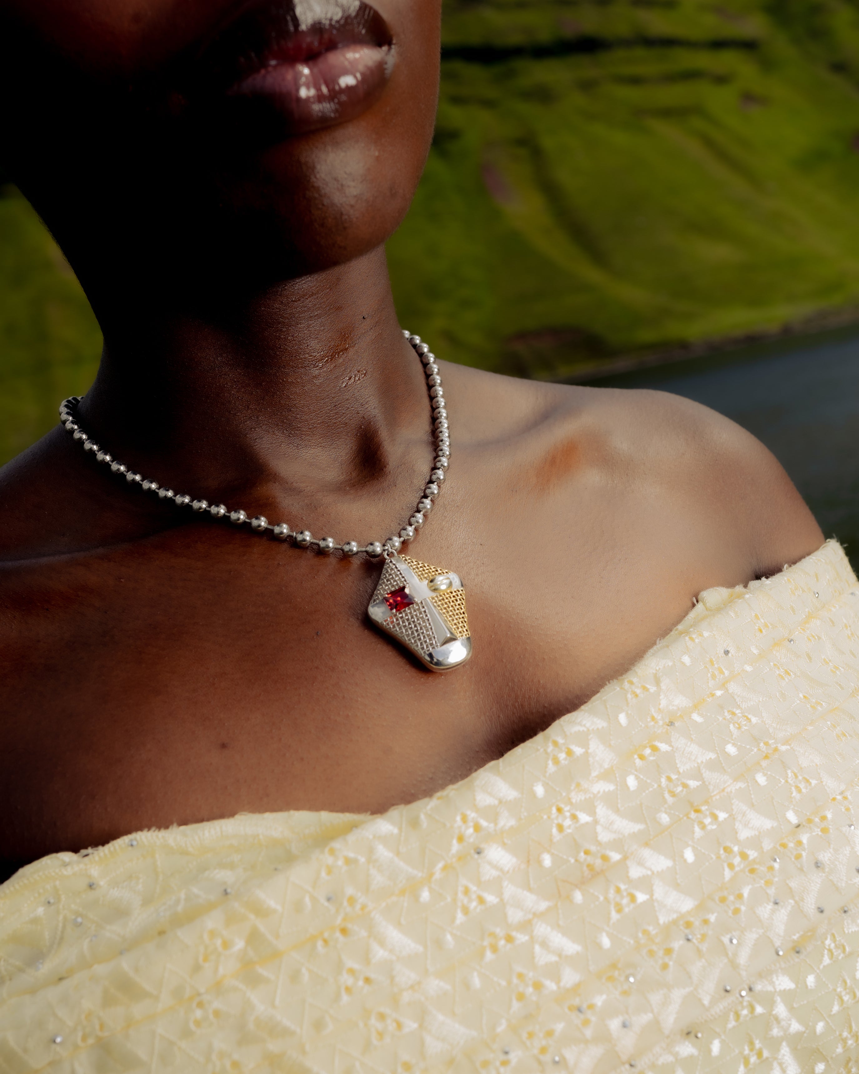 Close-up of a Senegalese woman wearing a Maison Nwar sculptural silver pendant necklace with red stone, styled in traditional fabric against the Welsh landscape.