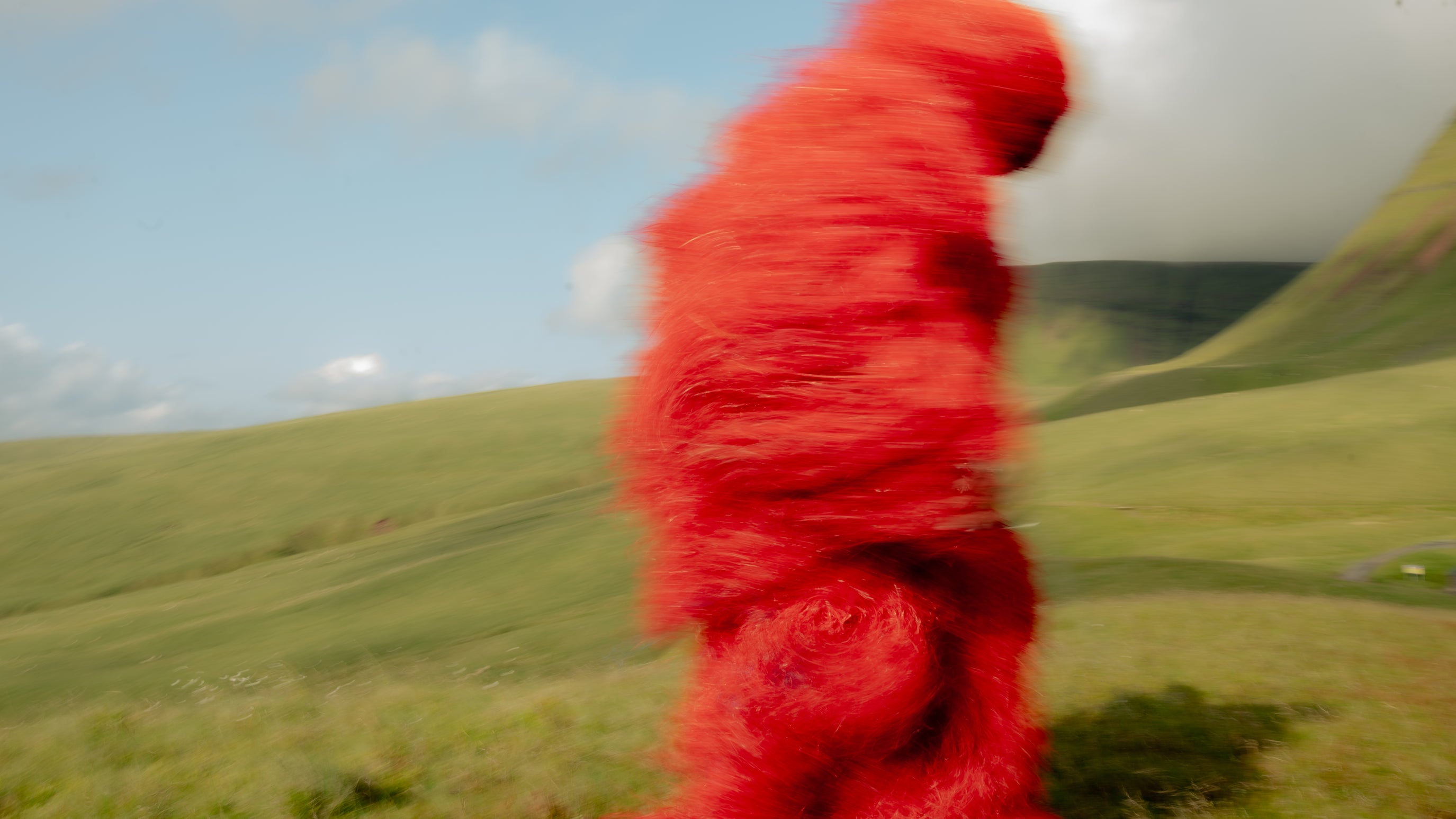 The Kankurang figure in a red costume walking through the green Welsh hills Maison Nwar cultural editorial shoot.